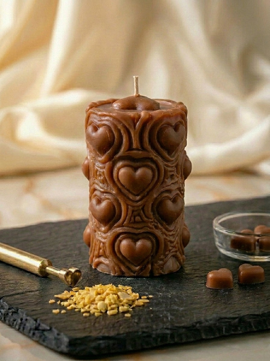Decorative candle with heart patterns on a dark surface with gold accents