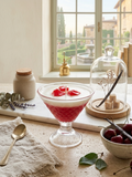 Red and white dessert in a glass bowl on a wooden table with a window view in the background.