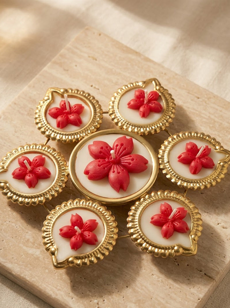 A set of six decorative brooches arranged in a flower-like cluster on a beige stone slab. Each brooch has a gold-toned scalloped frame, a white oval center, and a raised red flower motif.