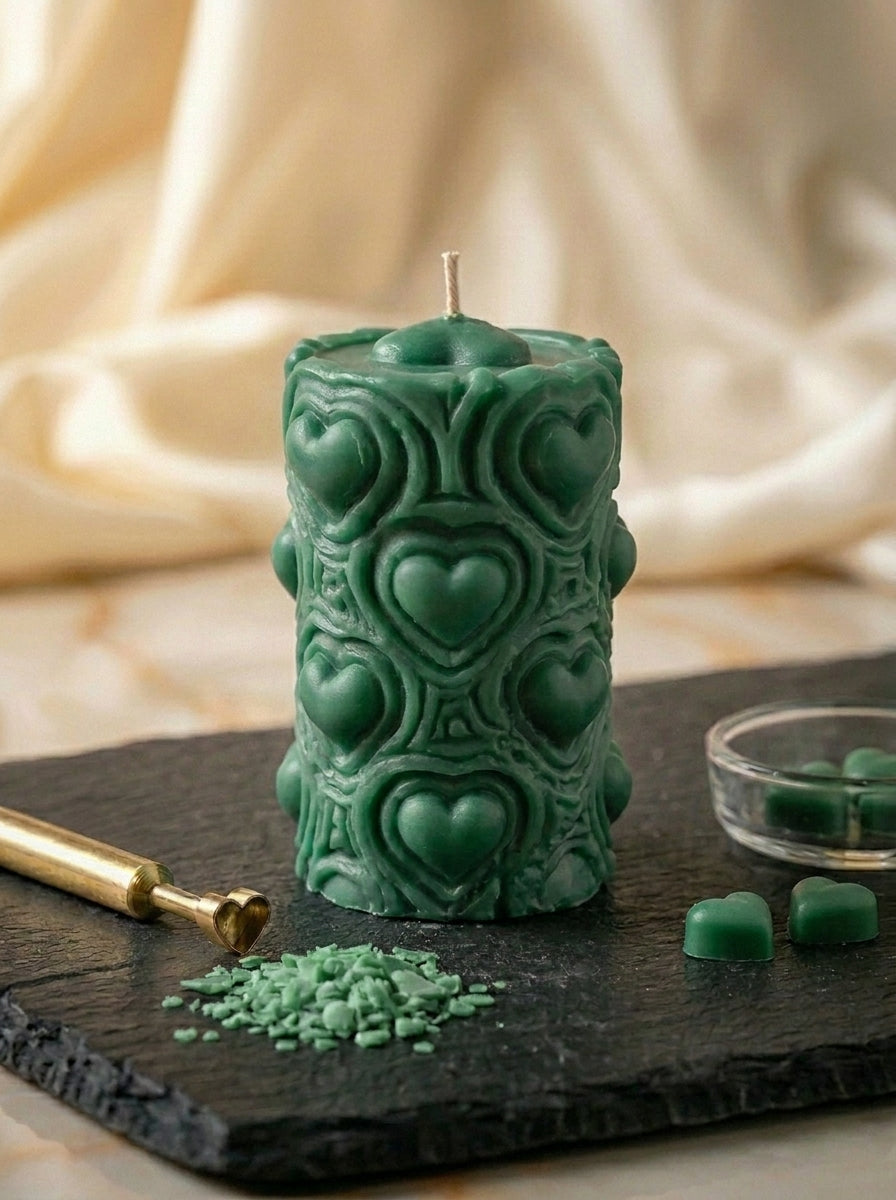 Decorative green candle with heart patterns on a dark surface with a beige fabric background