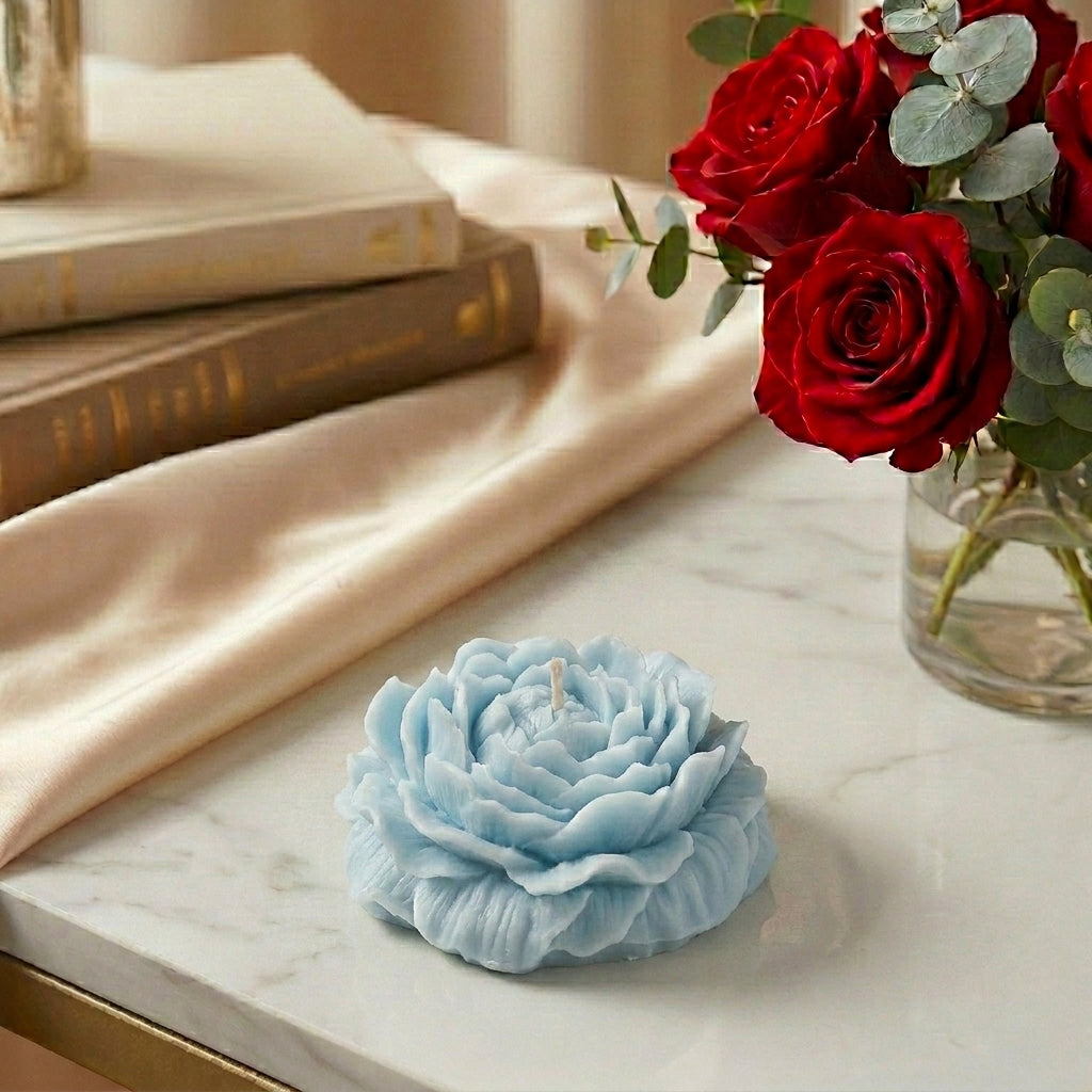 Blue flower-shaped candle on a marble surface with red roses in the background