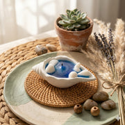 Decorative candle in a shell with a plant and stones on a woven mat