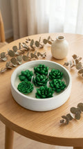 White bowl with green succulent-shaped objects on a wooden table with decorative leaves.