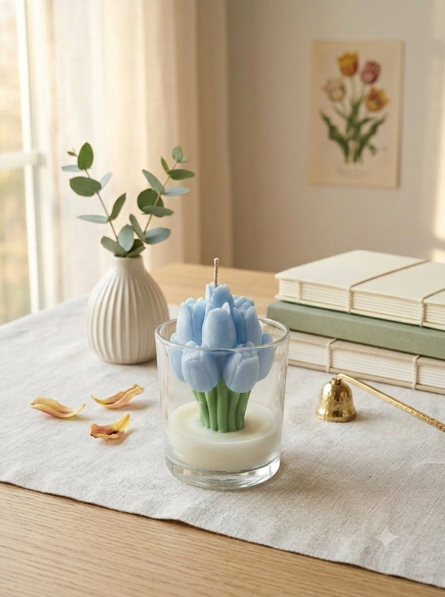 Candle shaped like a cactus in a glass container on a table with books and a vase in the background.